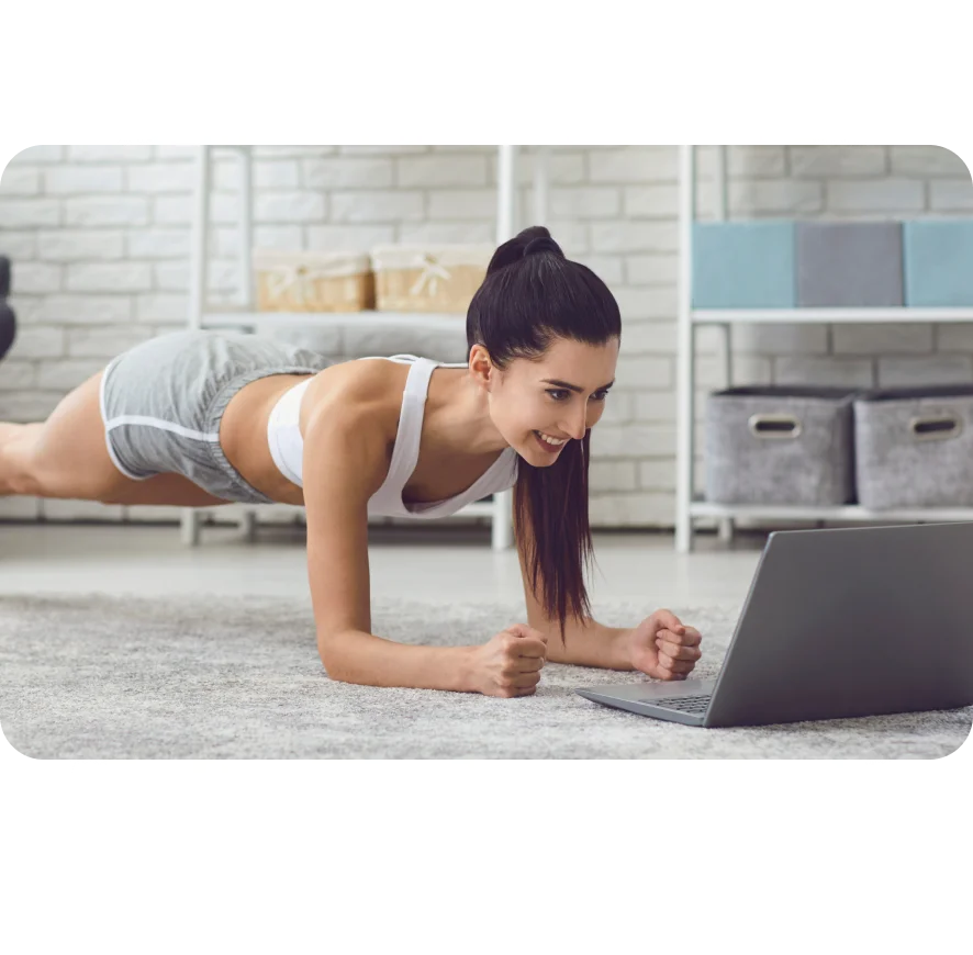 Smiling brunette girl in sportswear making a plank in front of laptop in her living room.